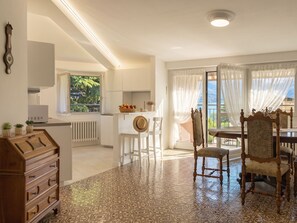A spacious kitchen with white cabinets, a dining area with a wooden table and chairs, and a view of the outdoors through large windows. - Balconi sulla Spiaggia by Interhome (Bellano)