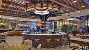 Zona de bar con un mostrador central, diversas opciones de asientos y un techo decorativo con lámparas colgantes.