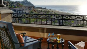 A balcony with a view of the ocean, a dining table with food and drinks, and a chair. - Junior Ocean View Suite with Sunset Views in Cabo (Cabo San Lucas)