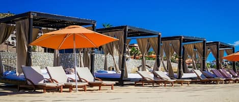 A beachside resort with sun loungers, orange umbrellas, and stone walls.