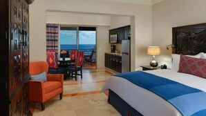 Habitación de hotel con cama, escritorio, silla, kitchenette y balcón con vistas.