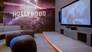 A cinema room with a large screen, a sofa, and a carpeted floor. - Junior Ocean View Suite with Sunset Views in Cabo (Cabo San Lucas)