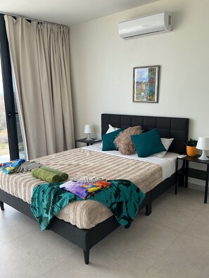 Ein Hotelzimmer mit Bett, Nachttisch, Lampe, Blumentopf und einem Fenster mit Vorhängen.