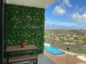 Ein Balkon mit Holztisch, roter Vase und Blick auf eine Wohngegend.