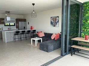 A modern living space with a kitchen, dining area, and a glass wall with a green plant backdrop. - Nice View Apt 8 - 2-BR apartment with AC on spectacular Mahuma hill (Willemstad)