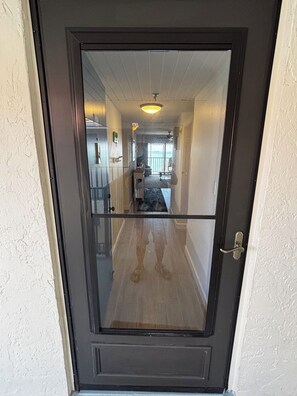 Une porte avec un panneau de verre, un ventilateur de plafond et une vue sur une pièce dotée d’une fenêtre et d’un balcon.