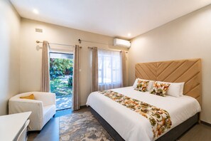 Una habitación de hotel con cama, una silla, una ventana y un equipo de aire acondicionado.