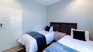 A bedroom with two beds, a wardrobe, and a nightstand.