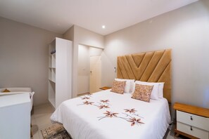A bedroom with a bed, bedside tables, a wardrobe, and a bathroom. - Cosmo Guest House (Victoria Falls)