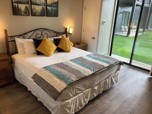Ein Schlafzimmer mit einem großen Bett, zwei Nachttischen, einer Wandlampe und einer Schiebetür zu einem Außenbereich.