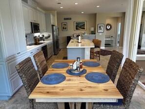 A modern kitchen with white cabinets, a central island, and a dining area with a wooden table and woven chairs. - Relaxing getaway next to award winning golf course (Nipomo)