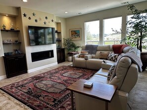 A living room with a large flat-screen TV, a beige sofa, a patterned rug, and a large window with a view. - Relaxing getaway next to award winning golf course (Nipomo)