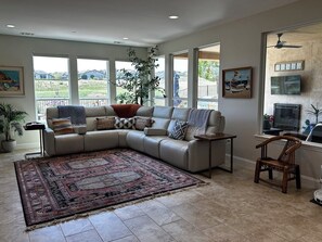Ein Wohnzimmer mit einer Eckcouch, einem großen Teppich und Blick ins Freie durch große Fenster.
