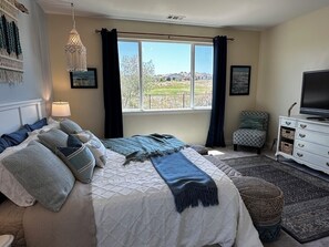 Ein Schlafzimmer mit einem Bett, einem Fernseher, einer Kommode und einem Fenster mit Blick ins Freie.