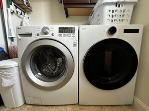 A laundry area with two washing machines, a trash bin, and a laundry basket. - Relaxing getaway next to award winning golf course (Nipomo)