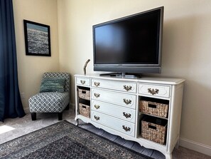 A living room with a flat-screen TV on a white cabinet, a patterned armchair, and a framed picture on the wall.