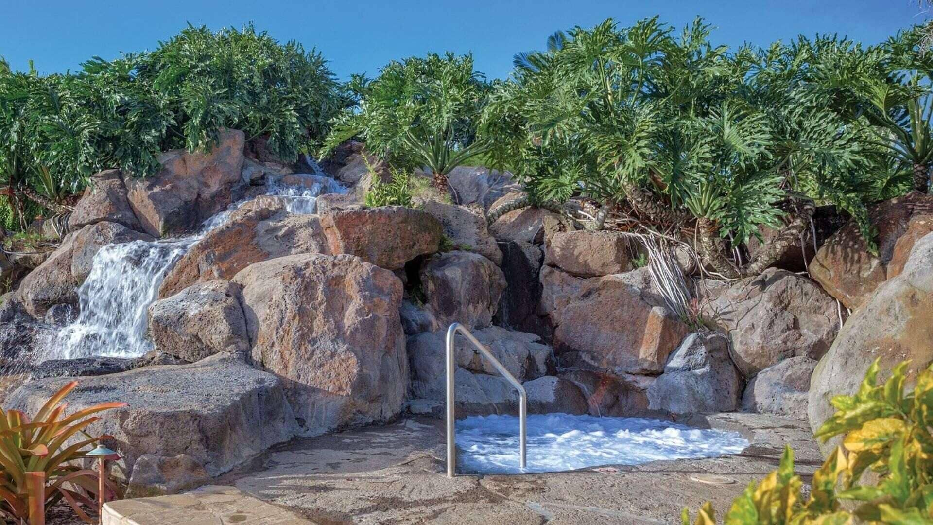 A natural rock pool with a waterfall, surrounded by lush greenery.