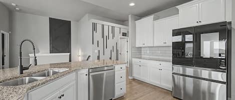 A modern kitchen with white cabinetry, stainless steel appliances, and a granite countertop.