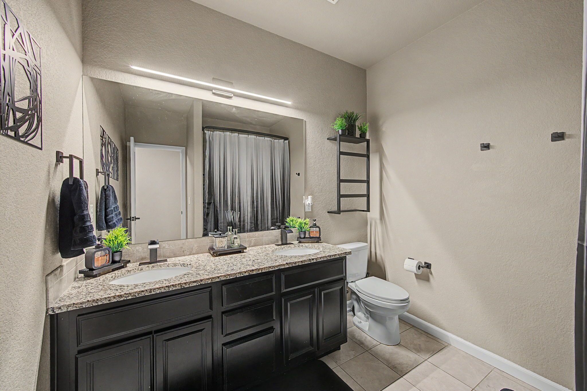 A modern bathroom with a granite countertop, black cabinets, a white toilet, and a large mirror.