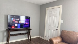 Un televisor de pantalla plana sobre un soporte de madera en una habitación con pared gris y una puerta cerrada.