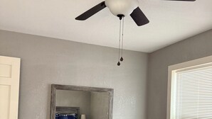 Un dormitorio con cama, cómoda, ventilador de techo y ventana con persianas.