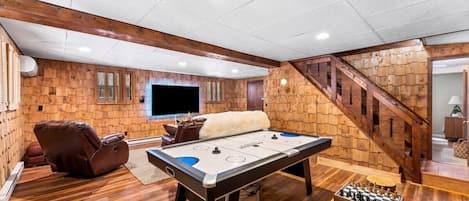 A cozy indoor space with a pool table, a foosball table, a massage chair, and a TV mounted on the wall.