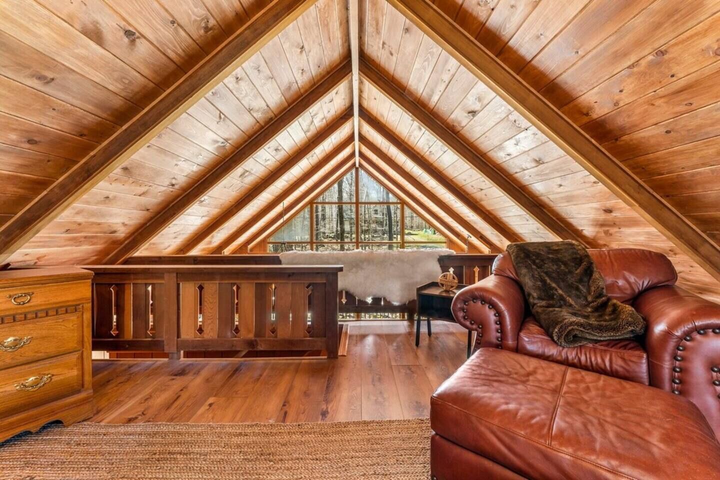 Slaapkamer in loftstijl met schuine plafonds, houten balken, een leren bank, een dressoir en uitzicht op het bos door grote ramen.