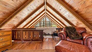 Slaapkamer in loftstijl met schuine plafonds, houten balken, een leren bank, een dressoir en uitzicht op het bos door grote ramen.