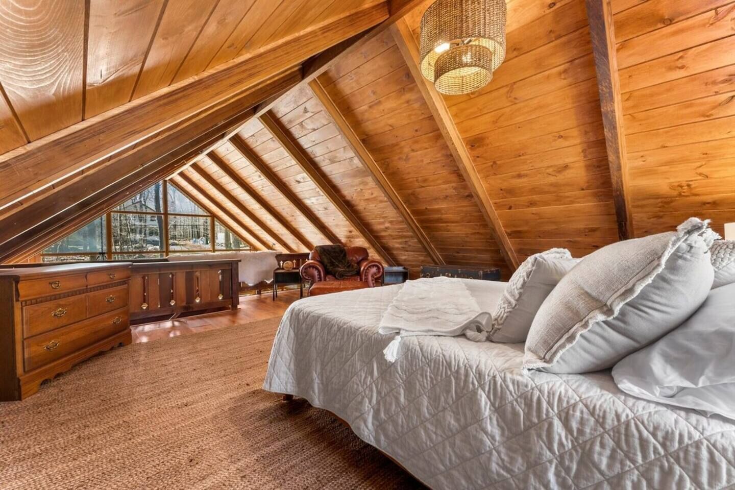 Un dormitorio en ático con techos altos, una cama grande, un aparador de madera y vistas por la ventana.