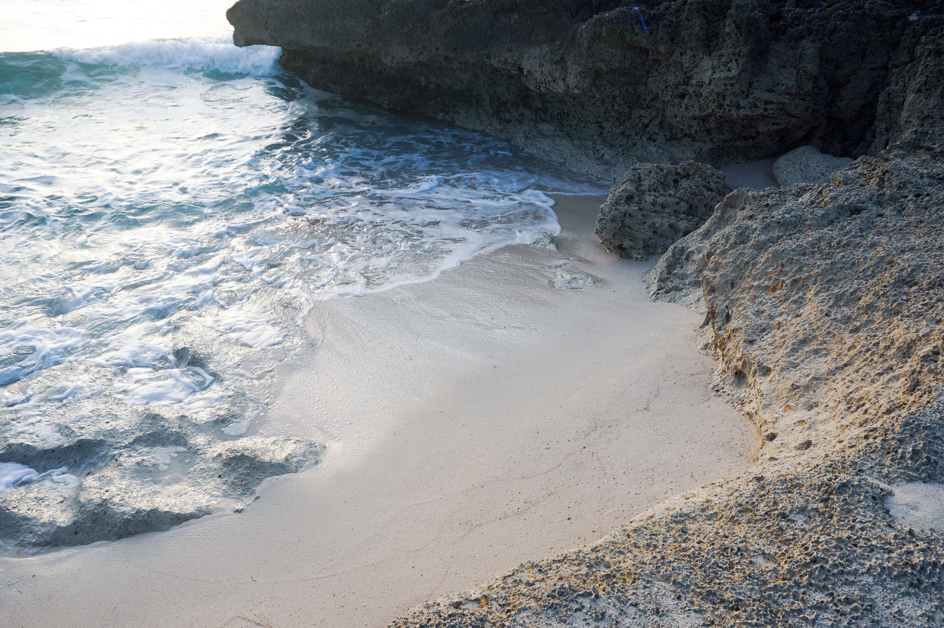 Ein Strand mit brechenden Wellen, einer felsigen Klippe und Sand.