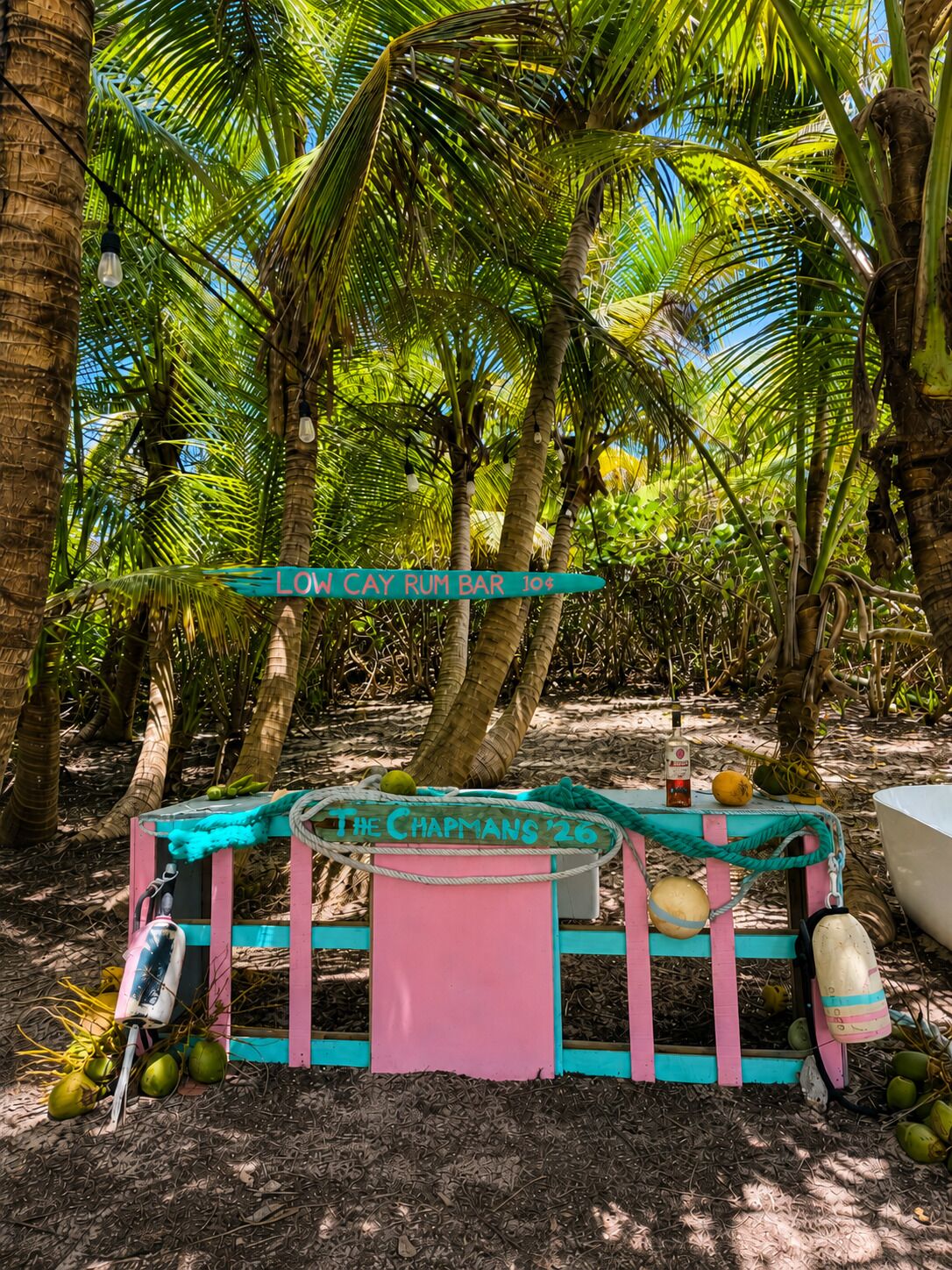 A rustic outdoor bar setup with a sign reading 'LOW CAY RUM BAR' and a vintage sign for 'THE CHAPMANS '26'.