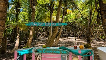 A rustic outdoor bar setup with a sign reading 'LOW CAY RUM BAR' and a vintage sign for 'THE CHAPMANS '26'.