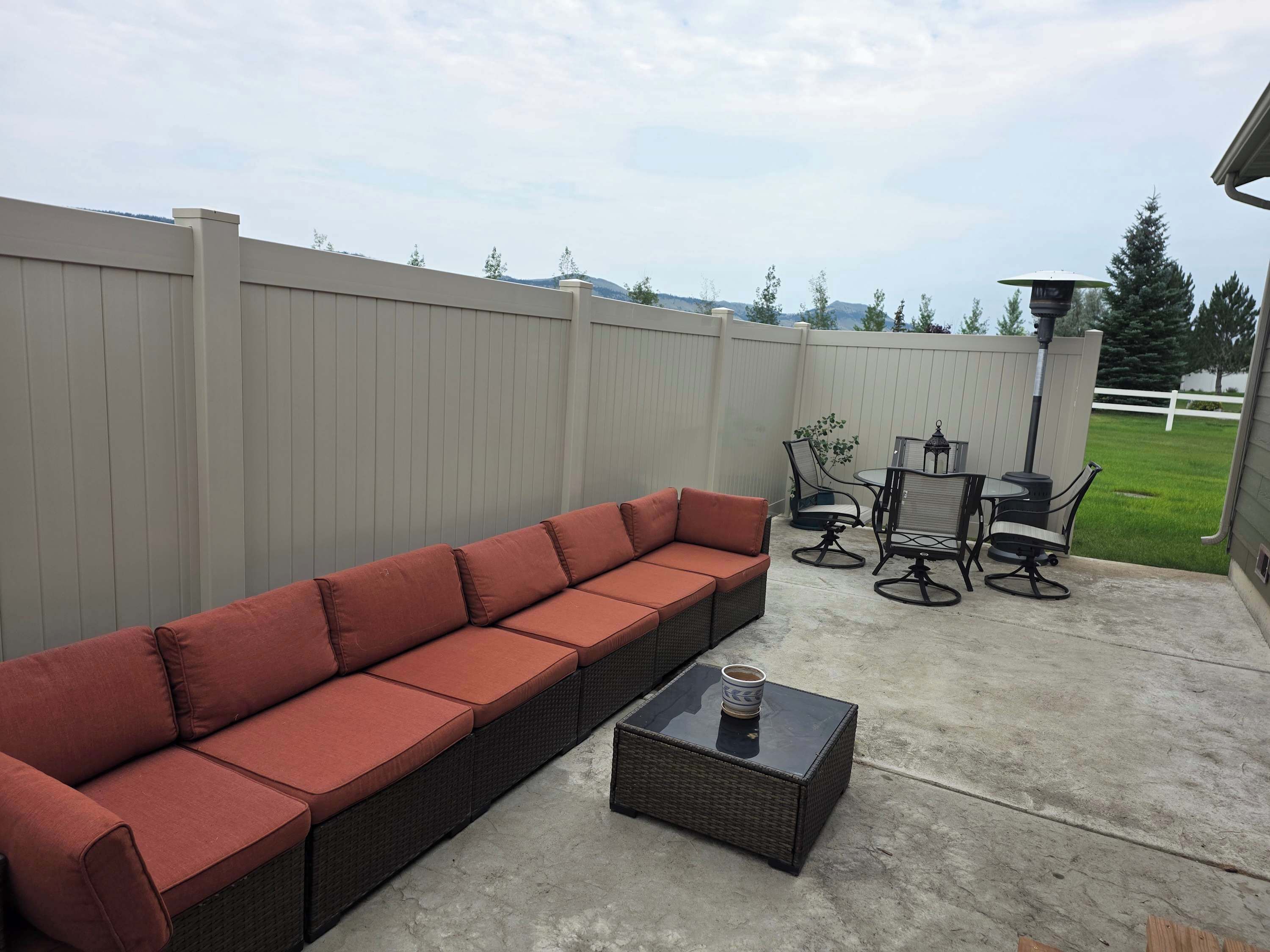 En patio med en lang, rød sofa, et rundt bord med stole og et lille firkantet bord med en kop.