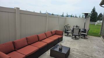 En patio med en lang, rød sofa, et rundt bord med stole og et lille firkantet bord med en kop.