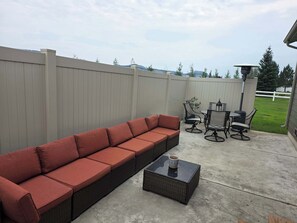 Eine Terrasse mit einer langen, roten Couch, einem runden Tisch mit Stühlen und einem kleinen, quadratischen Tisch mit einer Tasse.