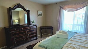 Un dormitorio con cama, cómoda, espejo, una mesita y ventana con cortinas.