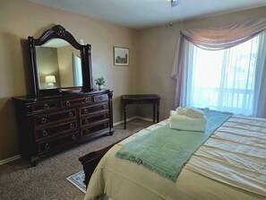 Ein Schlafzimmer mit einem Bett, einem Schminktisch, einem Spiegel, einem kleinen Tisch und einem Fenster mit Vorhängen.