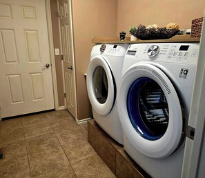 A laundry room with two front-loading washing machines, a door, and a tiled floor. - New Listing - Crested Wheat 3 Bedroom Retreat (East Helena)