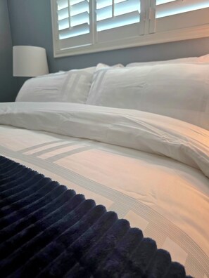 Una cama con sábanas blancas y un plaid azul oscuro.