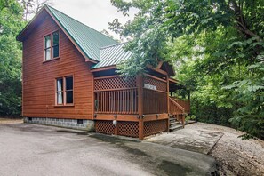 A wooden cabin with a metal roof, a wooden deck, and a stone foundation.