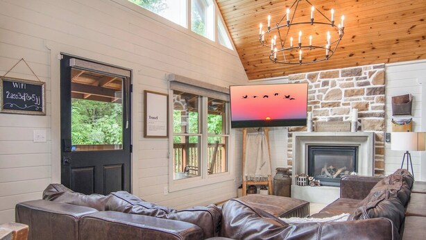 A cozy interior with a leather sofa, a fireplace, and a TV mounted on the wall. - Private Peaceful Cabin Near Dollywood w/ Hot Tub (Sevierville)