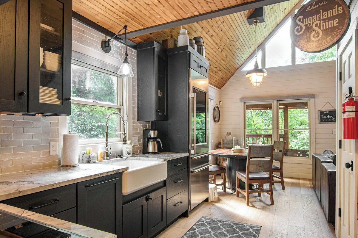 A kitchen with a wooden ceiling, a coffee maker, and a dining area with chairs and a table.