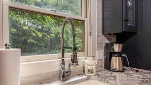 A kitchen with a stainless steel faucet, a coffee maker, and a window with a view of trees. - Private Peaceful Cabin Near Dollywood w/ Hot Tub (Sevierville)
