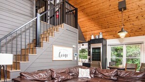A modern interior with a leather sectional sofa, a staircase, and a kitchen area. - Private Peaceful Cabin Near Dollywood w/ Hot Tub (Sevierville)