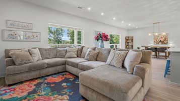 A spacious living area with a large sectional sofa, a colorful rug, and a dining area with a table and chairs.