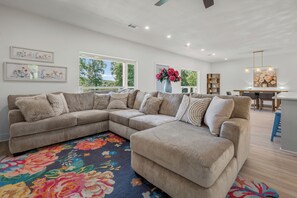 A spacious living area with a large sectional sofa, a colorful rug, and a dining area with a table and chairs. - Lux Waterfront Cabin - 2 King Ensuites, Large Covered Porch, Kayaks, Fire Pit! (Royal)