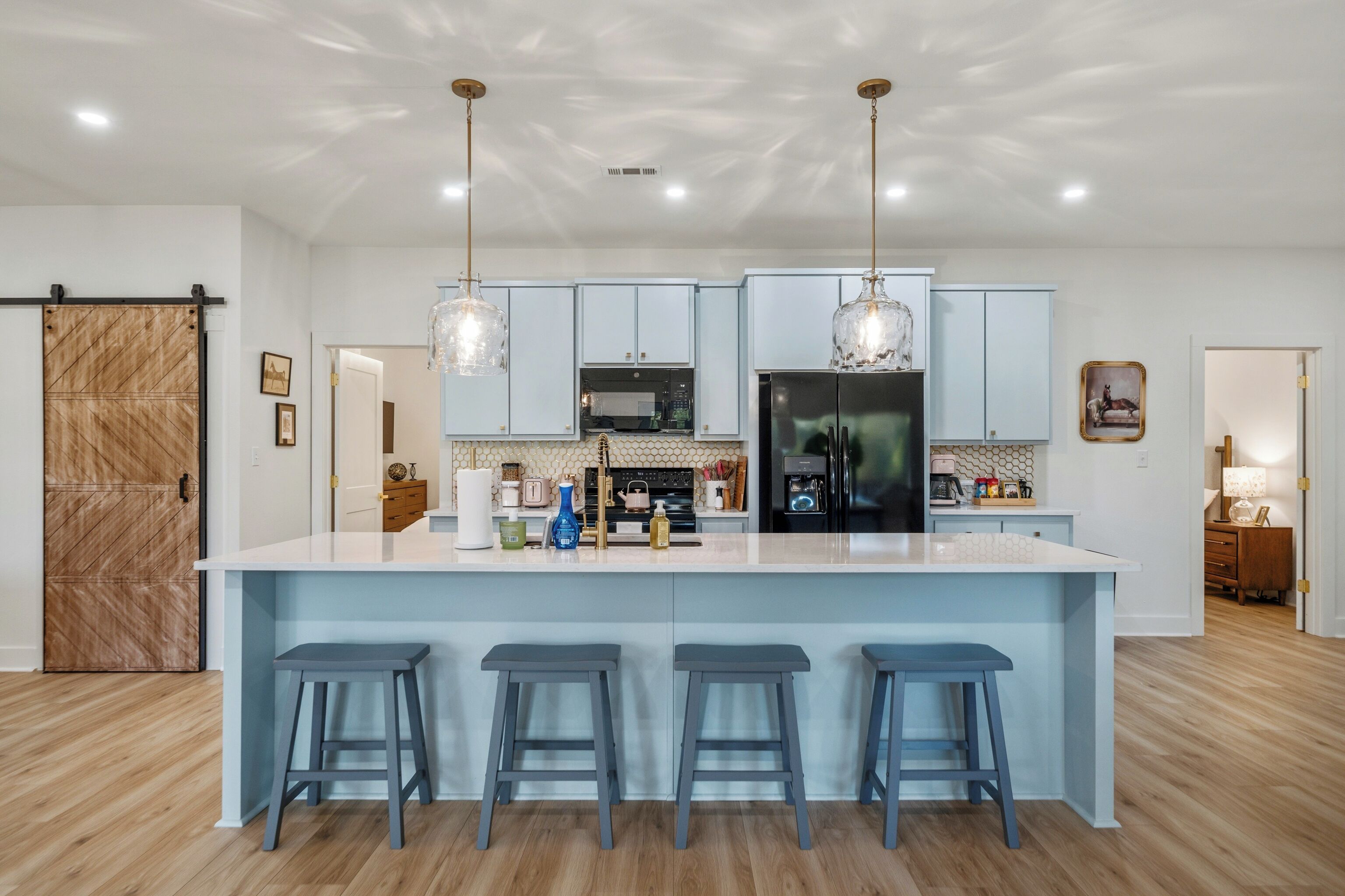 A modern kitchen with a central island, bar stools, pendant lighting, and a large refrigerator.