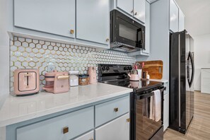 A modern kitchen with a microwave, oven, and refrigerator. There are cabinets with gold handles and a tiled backsplash. - Lux Waterfront Cabin - 2 King Ensuites, Large Covered Porch, Kayaks, Fire Pit! (Royal)