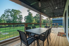 An outdoor patio with a table and chairs, overlooking a fenced yard with trees.