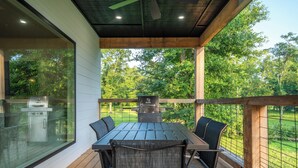 A covered outdoor dining area with a grill, a table, and chairs.